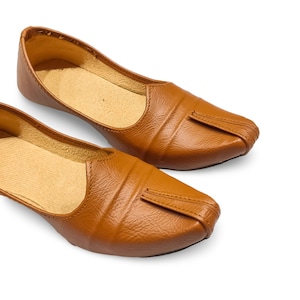 Puede incluir: Un par de zapatos sin cordones de cuero marrón. Los zapatos tienen un diseño de punta puntiaguda con un detalle cosido y una superficie texturizada. El interior presenta una plantilla de color beige claro. Los zapatos se muestran sobre un fondo blanco.