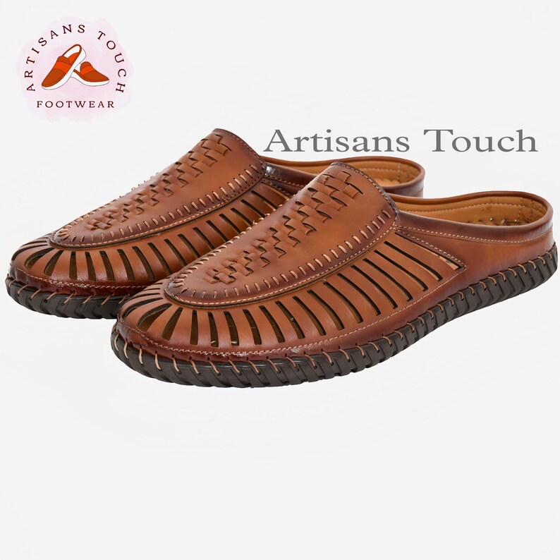 May include: A pair of brown leather sandals with a woven design and an open toe. The sandals have a brown leather strap across the top of the foot and a brown leather strap around the ankle. The sandals are made by Artisans Touch Footwear.