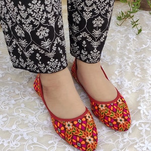 May include: A pair of red embroidered flat shoes with colorful floral patterns. The shoes have pointed toes and are made of a soft fabric.