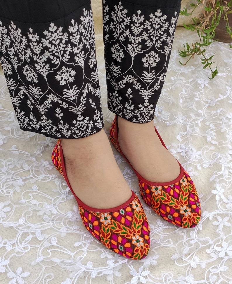 May include: A pair of red embroidered flat shoes with colorful floral patterns. The shoes have pointed toes and are made of a soft fabric.