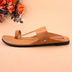 Op de afbeelding: Een paar bruine leren sandalen met een band over de bovenkant van de voet en een teenlus. De sandalen hebben een zwarte zool en de merknaam "Swas" is op de zool gedrukt.