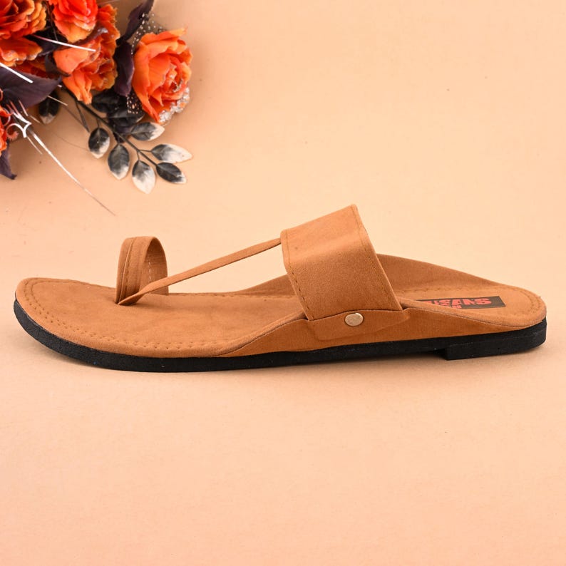 Op de afbeelding: Een paar bruine leren sandalen met een band over de bovenkant van de voet en een teenlus. De sandalen hebben een zwarte zool en de merknaam "Swas" is op de zool gedrukt.