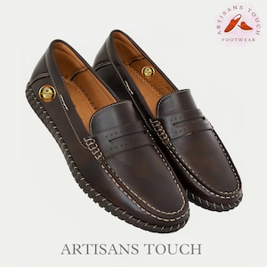 May include: A pair of brown leather loafers with a stitched edge and a decorative stitch detail on the vamp. The loafers have a leather sole and a comfortable fit. The brand name "Artisans Touch Footwear" is printed on the image.