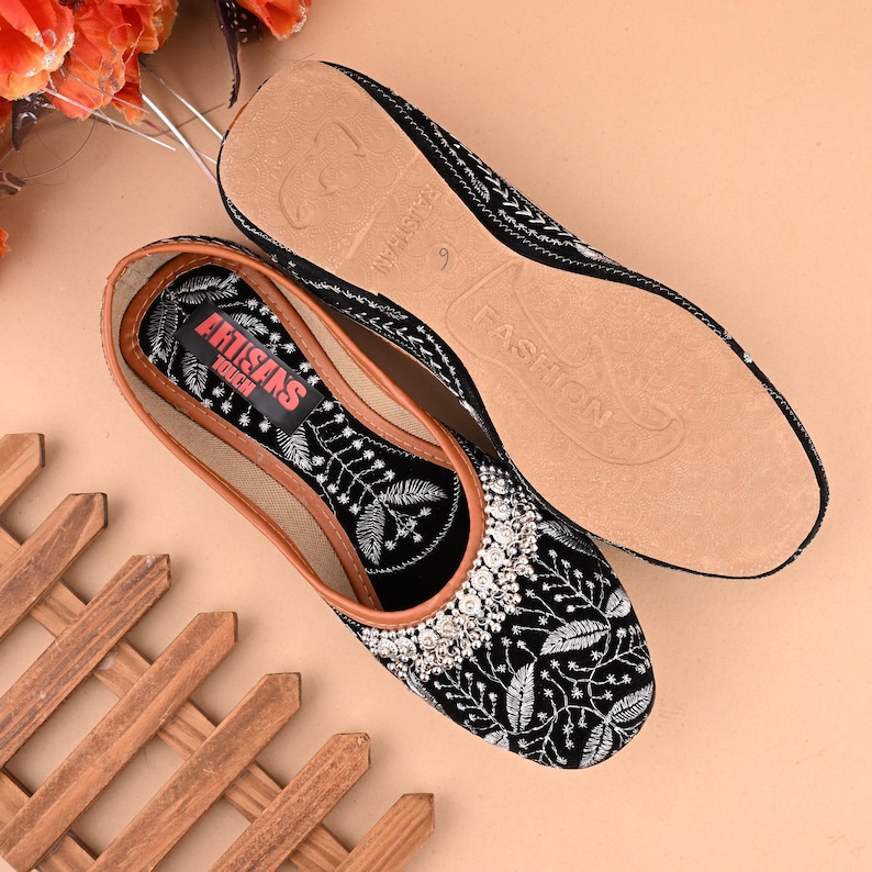 May include: Black velvet embroidered flat shoes with silver embellishments. The shoes have a brown leather insole with the text "ARTISANS" and "FASHION" printed on them.