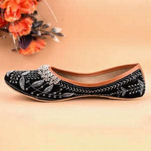 May include: Black embroidered flat shoes with silver embellishments. The shoes have a pointed toe and a low heel.