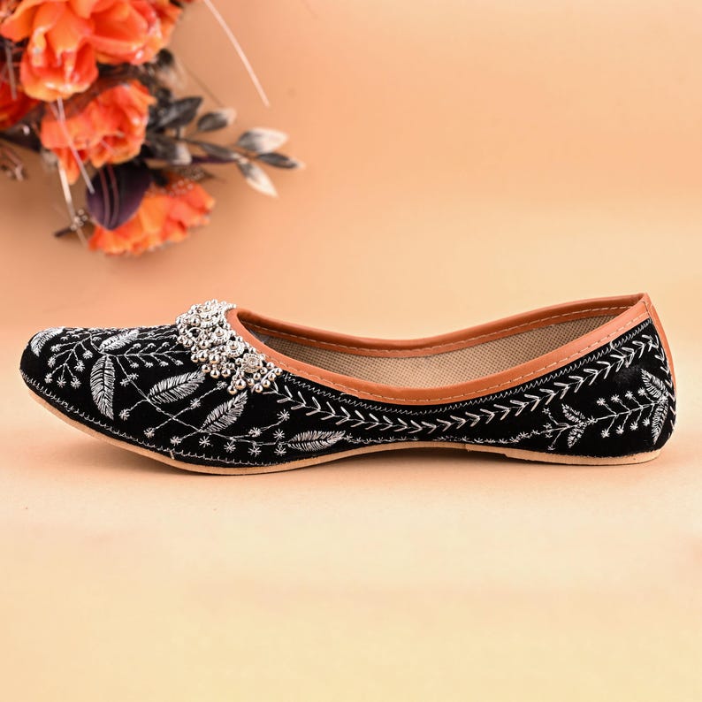 May include: Black embroidered flat shoes with silver embellishments. The shoes have a pointed toe and a low heel.