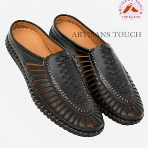May include: A pair of black leather sandals with a woven design and a brown stitching detail. The sandals have an open toe and a closed heel. The sandals are made by Artisans Touch Footwear.