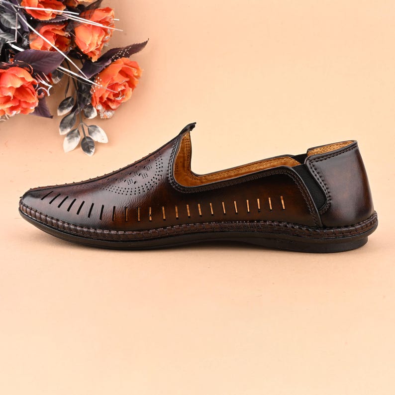 K&ouml;nnte beinhalten: Braune Lederschuhe zum Hineinschl&uuml;pfen mit perforiertem Design und einem schwarzen elastischen Riemen an der Ferse.