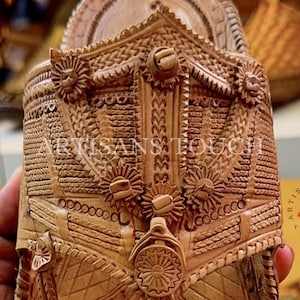 May include: Close-up of a handcrafted, light brown wooden sandal with intricate carved details. The sandal features floral and geometric patterns, with the text "ARTISANS TOUCH FOOTWEAR" visible on the side.
