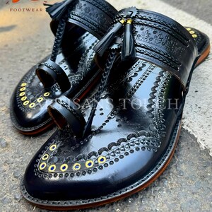 May include: A pair of black leather sandals with intricate embossed designs and decorative tassels. The sandals feature a toe loop and a strap across the top of the foot. Gold and blue accents are visible. The sandals are labeled "ARTISANS TOUCH FOOTWEAR".
