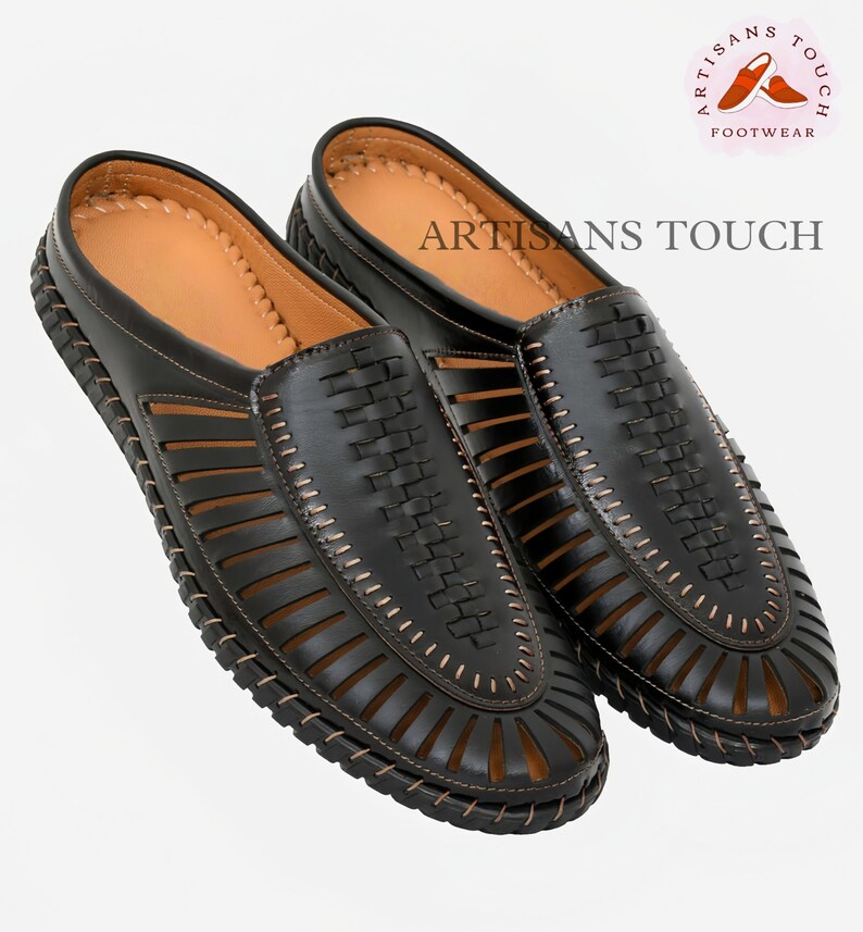 May include: A pair of black leather sandals with a woven design and a brown stitching detail. The sandals have an open toe and a closed heel. The sandals are made by Artisans Touch Footwear.