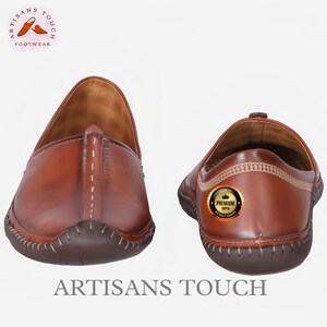 May include: Two brown leather slip-on shoes. The shoes have a rounded toe and a stitched sole. The image includes the text "ARTISANS TOUCH FOOTWEAR" and a "Premium" quality guarantee badge.