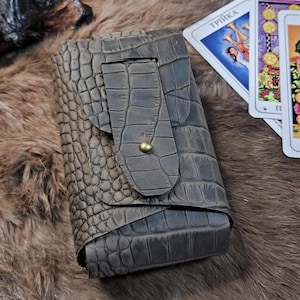May include: A brown leather card case with a flap closure and a crocodile embossed pattern. The case has a brass button closure on the flap.