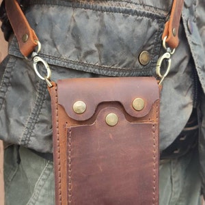May include: A brown leather crossbody bag with a flap closure and a small pocket on the front. The bag has a strap with a metal clasp.