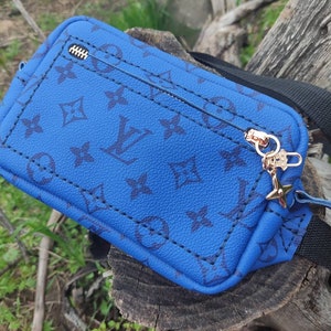 May include: A blue crossbody bag with a black strap and gold zipper pull. The bag features a black and white monogram pattern.