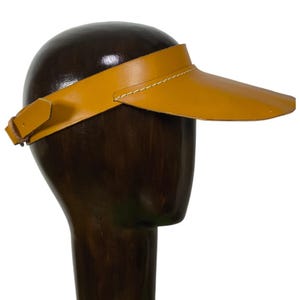 Könnte beinhalten: Ein Visier aus braunem Leder mit einer Naht um den Rand. Das Visier befindet sich auf einem hölzernen Mannequin-Kopf.