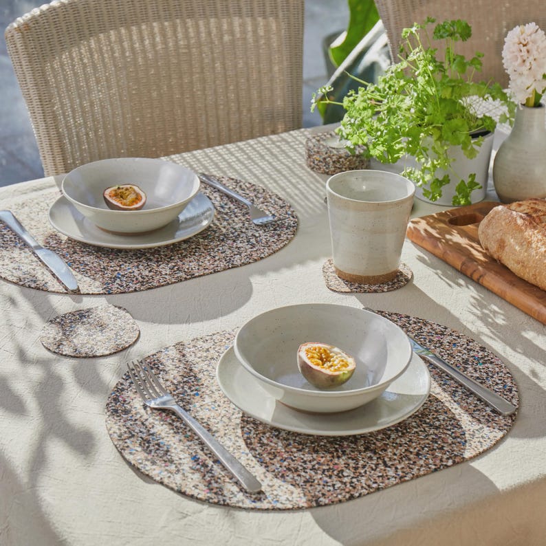 Peut inclure: Un service de table compos&eacute; de deux sets de table ovales au motif multicolore mouchet&eacute;, chacun supportant un bol et une assiette en c&eacute;ramique blanche. Une fourchette et un couteau en argent sont pos&eacute;s sur chaque set. Un gobelet en c&eacute;ramique blanche, une planche &agrave; d&eacute;couper en bois avec du pain et une plante en pot sont &eacute;galement pr&eacute;sents.