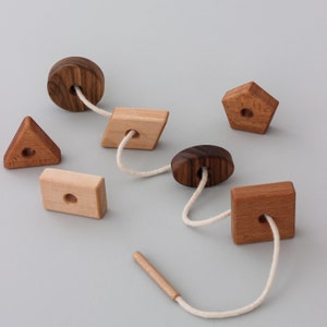 May include: A wooden toy with different shapes and a white string threaded through the holes. The shapes include a circle, a square, a triangle, a rectangle, and a pentagon. The toy is made of natural wood and has a rustic look.