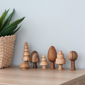 Könnte beinhalten: Ein Set aus sieben Holzspielzeugbäumen in verschiedenen Formen und Größen. Die Bäume sind aus Naturholz gefertigt und haben einen rustikalen, handgefertigten Look.