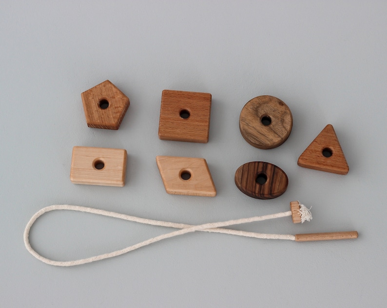 May include: A set of wooden shapes with holes in the center, strung on a white cord. The shapes include a circle, a triangle, a square, a rectangle, a pentagon, and an oval. The shapes are made of different types of wood, including light and dark wood.