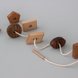 May include: A wooden toy with different shapes strung together with a white cord. The shapes include a triangle, a circle, a rectangle, a diamond, an oval, and a square.