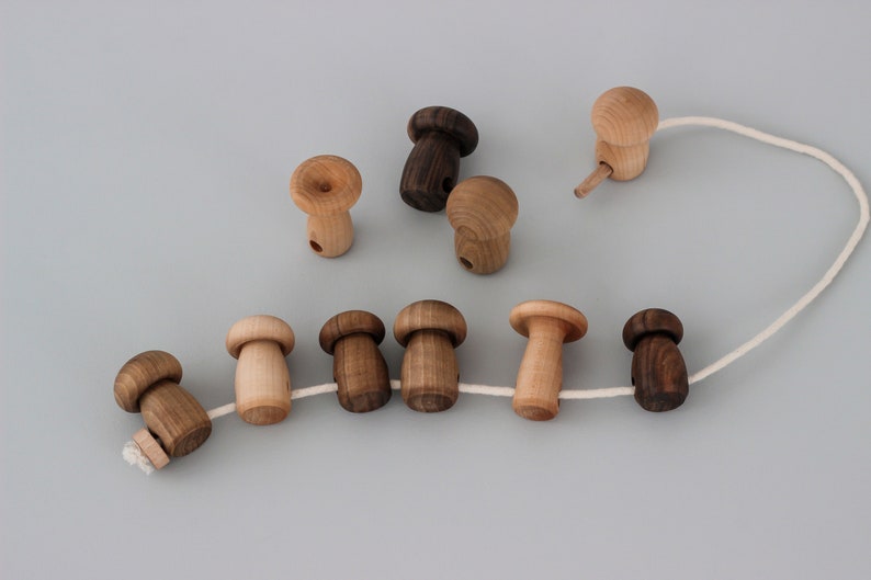 May include: A string of wooden mushroom-shaped beads in various shades of brown, connected by a white string. The beads are strung together in a line, with the string extending out on either side.