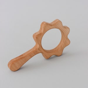 May include: A wooden hand mirror with a sun-shaped frame. The mirror is made of light brown wood and has a smooth, polished finish.