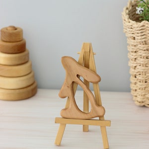 May include: A wooden rabbit sculpture on a small wooden easel. The rabbit is carved in a simple, abstract style and has a light brown colour.