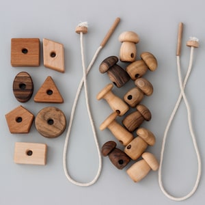 May include: A set of wooden toys for children, including geometric shapes and mushroom-shaped pieces. The toys are strung on two white cords.