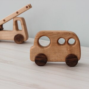 Op de afbeelding: Twee houten speelgoedvoertuigen, een brandweerwagen met een ladder en een bus. Beide voertuigen zijn gemaakt van lichtbruin hout met donkerbruine wielen.