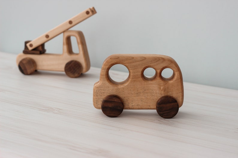 Op de afbeelding: Twee houten speelgoedvoertuigen, een brandweerwagen met een ladder en een bus. Beide voertuigen zijn gemaakt van lichtbruin hout met donkerbruine wielen.