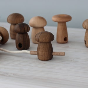 May include: A set of wooden mushroom toys with a string connecting them. The mushrooms are different sizes and colors, and some have holes in the top.