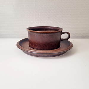 Peut inclure: Un ensemble tasse et soucoupe en céramique marron. La tasse a une anse et repose sur une soucoupe assortie. L'ensemble a un aspect tacheté et texturé. La couleur est un marron profond et terreux.