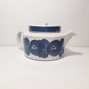 Könnte beinhalten: Eine weiße Keramik-Teekanne mit blauem Blumenmuster und einem einfarbigen blauen Deckel. Die Teekanne hat einen Griff und einen Ausguss. Das Blumenmuster bildet einen auffälligen Kontrast zum weißen Hintergrund.