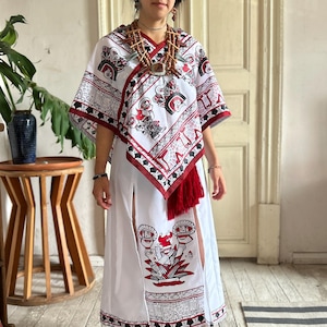 Peut inclure: Robe blanche ornée de motifs rouges et noirs, avec un haut de style poncho assorti et une frange rouge. L'ensemble comprend un collier de perles et un coiffe décorative. La robe a des fentes latérales.