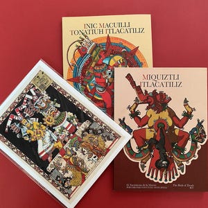Puede incluir: Tres libros y una impresión enmarcada con ilustraciones de inspiración azteca. Los libros tienen títulos en español y presentan ilustraciones coloridas de figuras y símbolos. La impresión es cuadrada con un diseño detallado y multicolor.