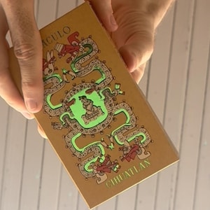 May include: A rectangular tan box featuring a central green illustration of a seated figure surrounded by a winding serpent design. The text ACULO is printed in the upper left corner and CIHUATLAN is printed in the lower right corner in green.