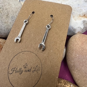 May include: A pair of silver wrench earrings on a brown card with the text "Holly and Lili" printed on it.