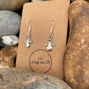 May include: Silver angel wing earrings displayed on a brown card with the text "Holly and Lili" printed on it.