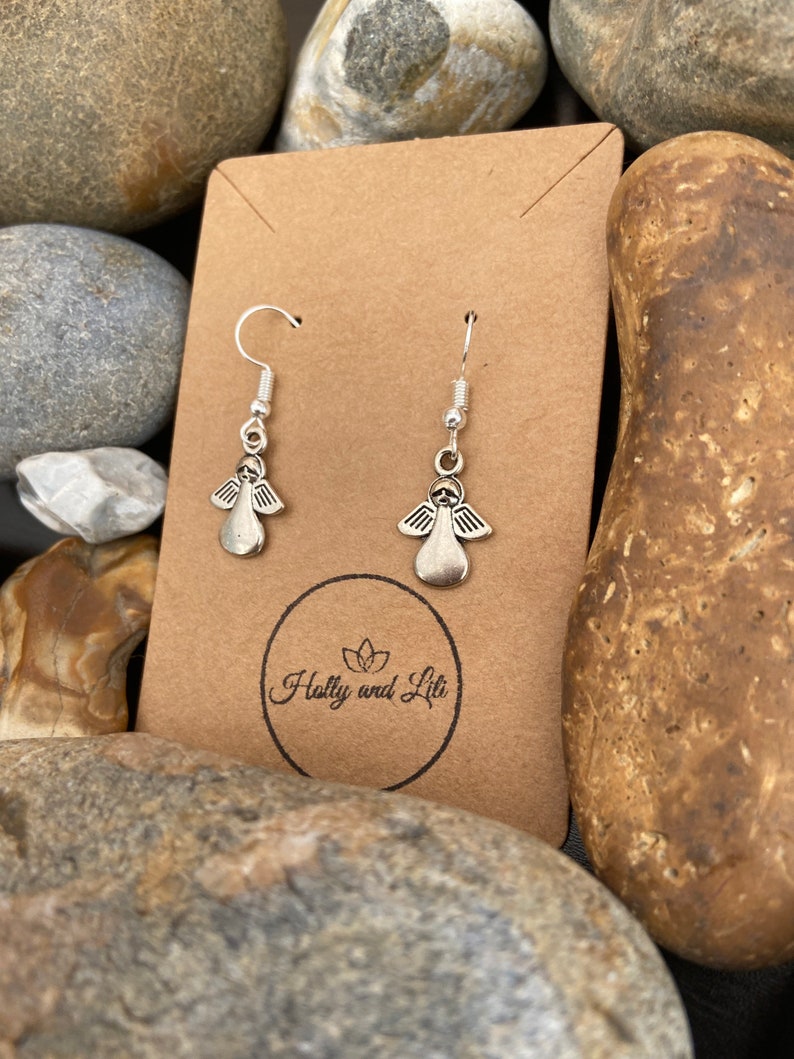 May include: Silver angel wing earrings displayed on a brown card with the text "Holly and Lili" printed on it.
