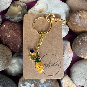 May include: Gold pineapple keychain with a blue gem charm and the letter "E" on a brown card with the text "Holly and Lili".