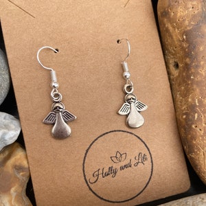 May include: A pair of silver angel dangle earrings on a brown card with the text "Holly and Lili" printed on it.