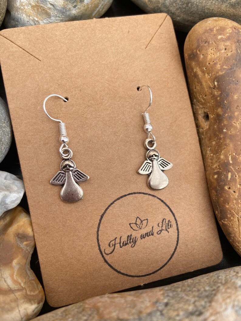 May include: A pair of silver angel dangle earrings on a brown card with the text "Holly and Lili" printed on it.