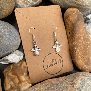 May include: A pair of silver angel dangle earrings on a brown card with the text "Hully and Lit" printed on it.