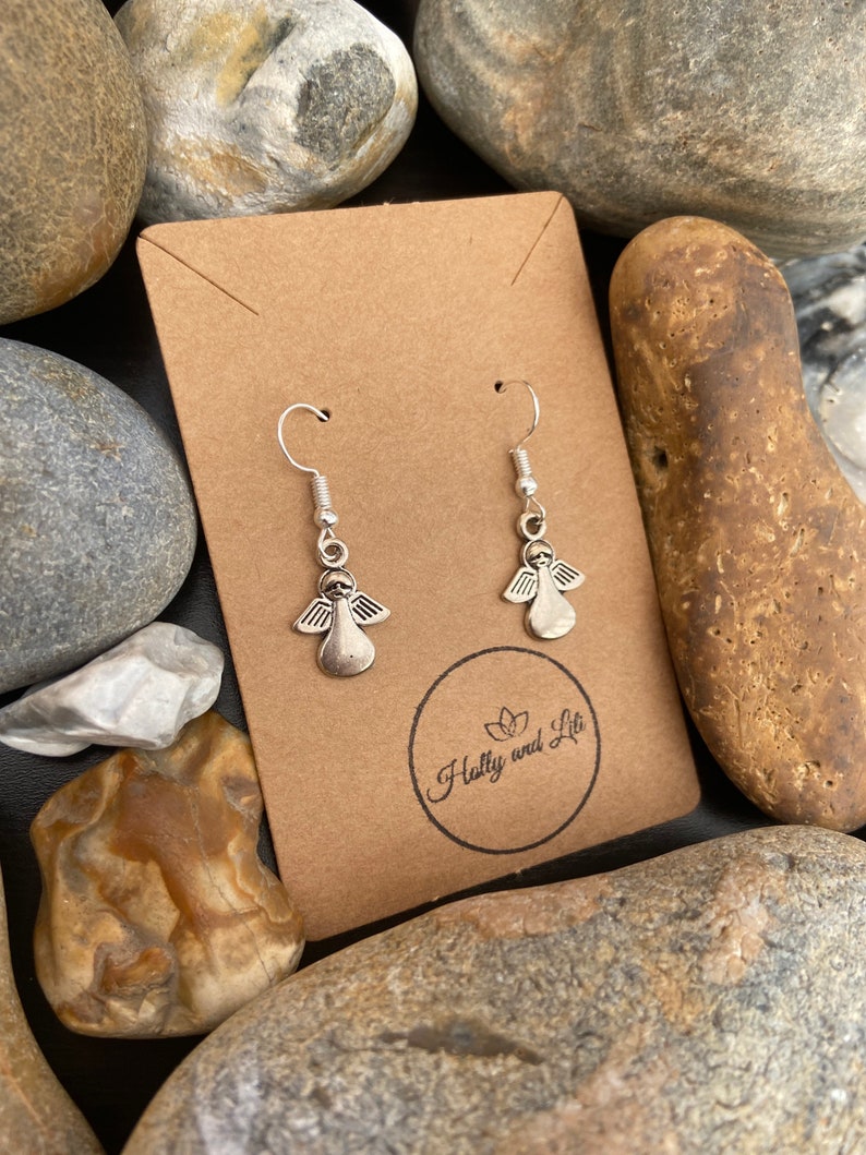 May include: A pair of silver angel dangle earrings on a brown card with the text "Hully and Lit" printed on it.