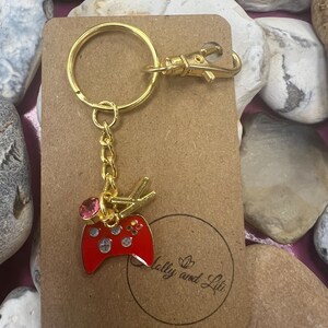 May include: Gold keychain with a red video game controller charm, a pink rhinestone, and a gold split ring. The keychain is attached to a brown card with the text "Molly and Lili" in gold lettering.