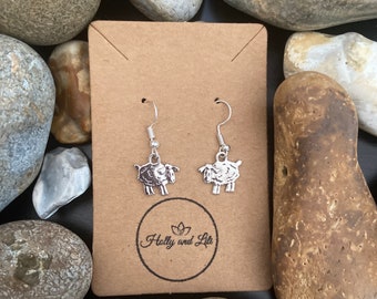 May include: Silver dangle earrings featuring a small sheep charm. The earrings are displayed on a brown card with the text "Holly and Lil" printed on it.