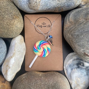 May include: A silver chain necklace with a colorful lollipop charm and a blue crystal charm. The necklace is displayed on a brown card with the text "Holly and Life" printed on it.