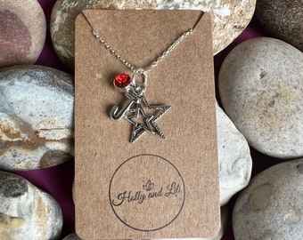May include: A silver necklace with a star charm and a red crystal. The necklace is on a brown card with the text "Holly and Lili" in a circle.
