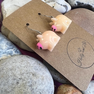 May include: A pair of pig-shaped earrings with pink details. The earrings are on a brown card with the text "H&B crafty and stuff" in a circle.